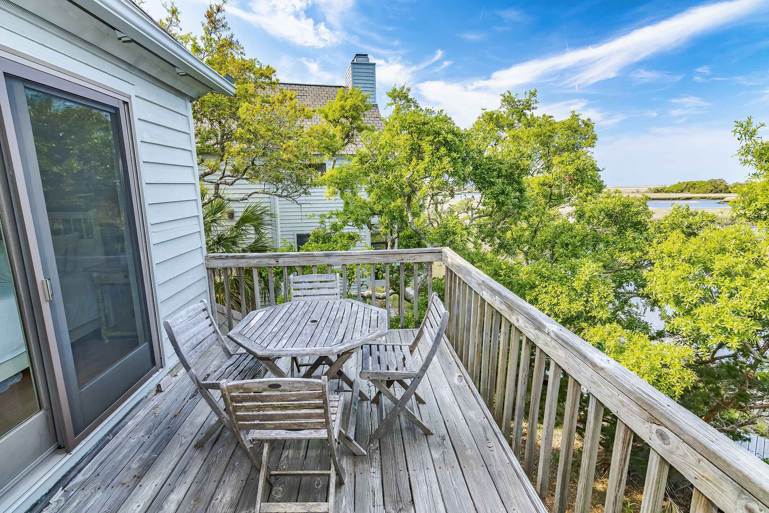 Une terrasse en bois avec une table et des chaises, donnant sur une étendue d’eau et des arbres.