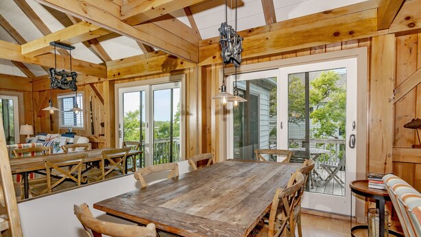 Un comedor de madera con una mesa grande y sillas, un banco y una pequeña mesa con una lámpara.