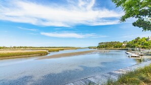Un río con un muelle de madera y un bote, rodeado de vegetación y un cielo despejado.
