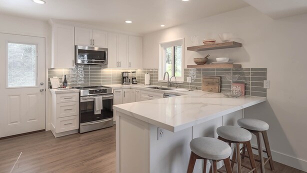 Una cocina moderna con muebles blancos, electrodomésticos de acero inoxidable, una isla grande con taburetes y un ventanal que proporciona luz natural.