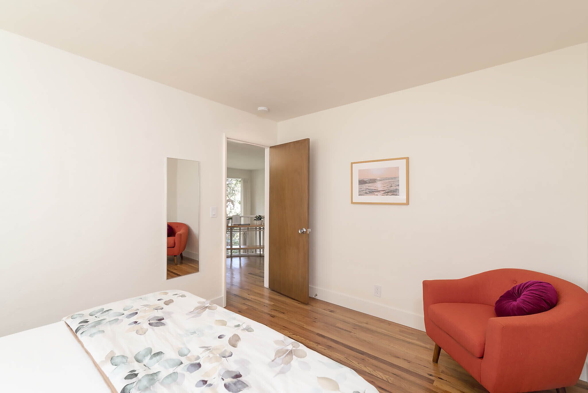A bedroom with a bed, a chair, a door, and a hallway leading to another room.