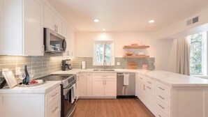 Una cocina moderna con armarios blancos, electrodomésticos de acero inoxidable y un amplio ventanal que proporciona luz natural.