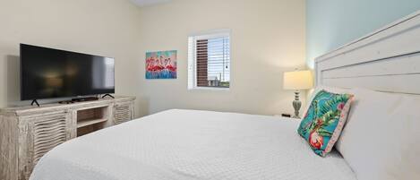 A bedroom with a large bed, a television on a wooden cabinet, a window with blinds, and a painting on the wall.