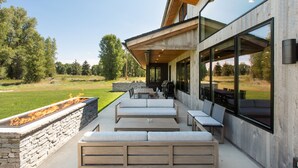 Eine moderne Außenpatio mit Steinmauern, Holzmöbeln und großen Fenstern mit Blick auf eine grüne Landschaft.