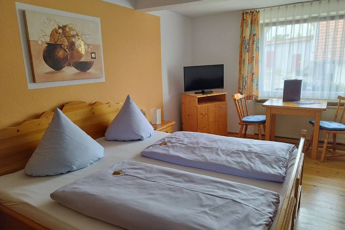 Hotellihuone, jossa on sänky, työpöytä, televisio ja ikkuna, jossa on verhot.