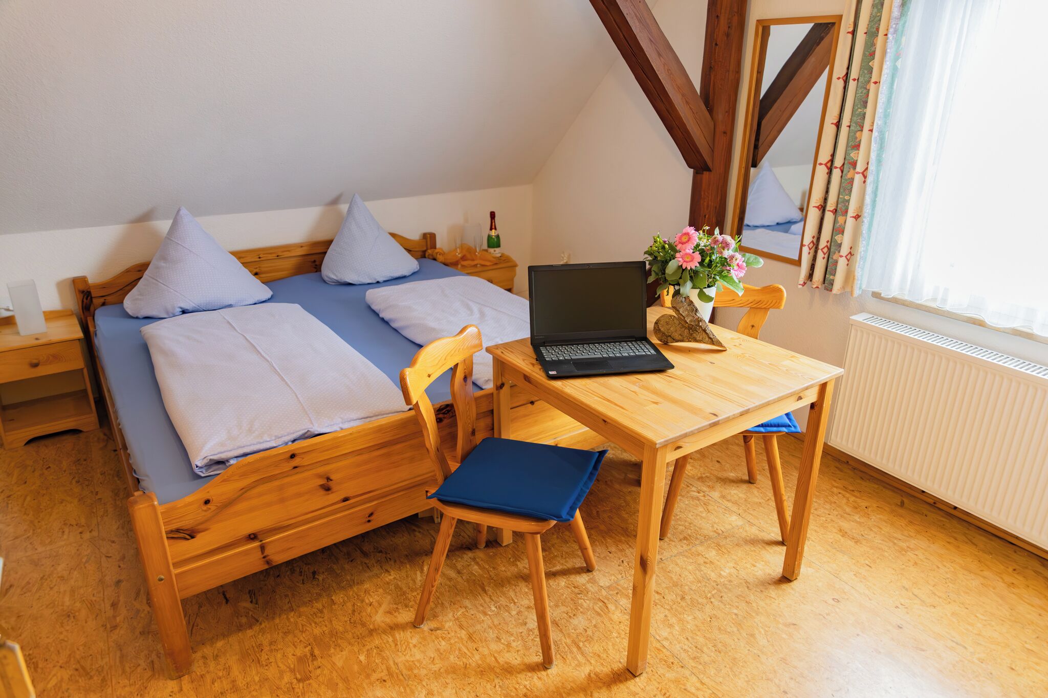 Un lit en bois avec des oreillers et un ordinateur portable posé sur une table en bois.