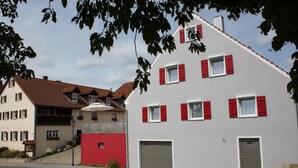 A residential building with a red facade, multiple windows with shutters, and a garage door. - Ferienhof Hofer (Absberg)