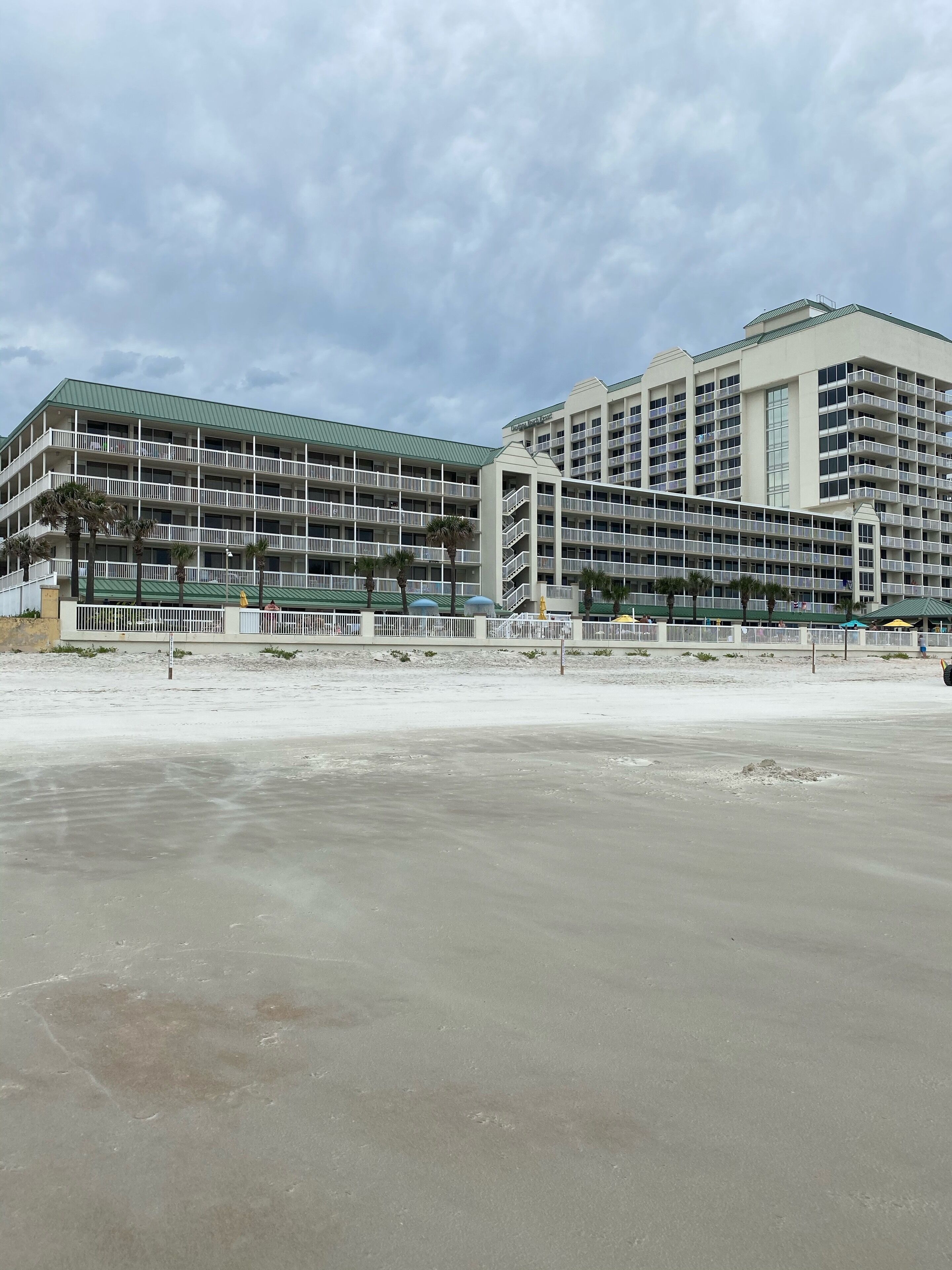 A large hotel with multiple floors and balconies, located near a beach.