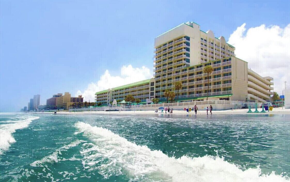 Un hôtel à plusieurs étages, doté de balcons, situé près d’une plage où l’on peut voir les vagues.