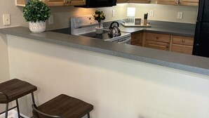 Una cucina con mobili in legno, un forno a microonde, un piano cottura e un lavello. Ci sono tre sgabelli al bancone.