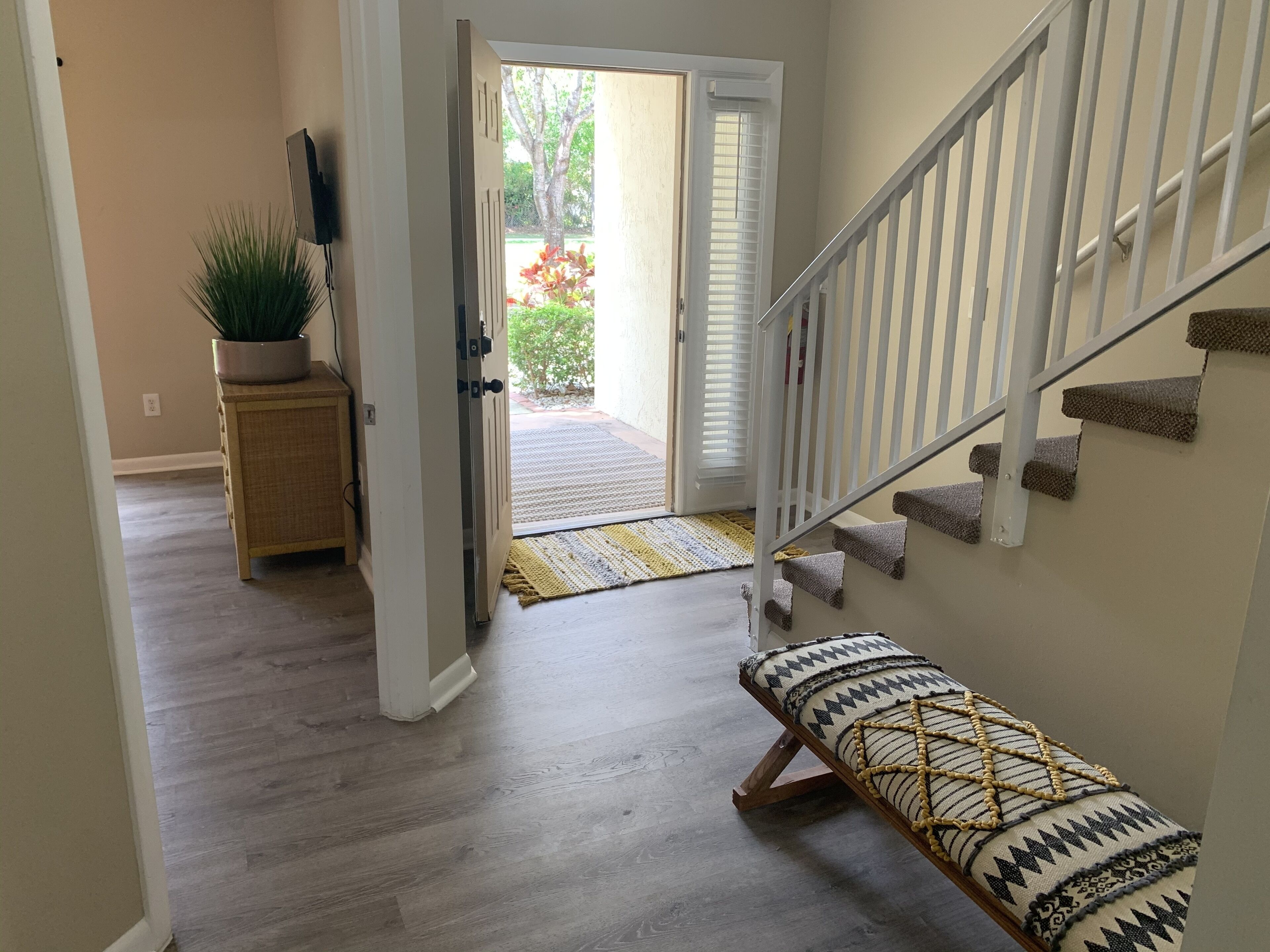 A hallway with a wooden bench, a potted plant, and a staircase leading to an outdoor area with a door and a window.