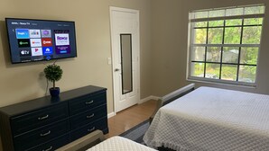 Camera da letto con due letti, una TV a parete, un comò e una finestra vista verde.