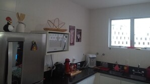 Une cuisine compacte équipée d’un réfrigérateur, d’un four à micro-ondes, d’une machine à café et d’une fenêtre laissant entrer la lumière naturelle.