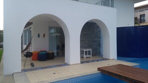 Un espace piscine extérieur moderne, doté d’une terrasse en bois, de deux arcades et d’un mur en pierre.
