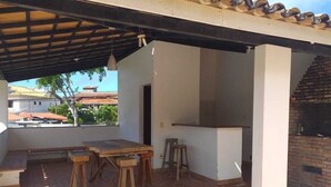 Un patio al aire libre con piso de ladrillo, una mesa de madera y una zona de barbacoa.