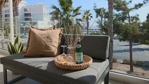 En balkong med ett flätat brickbord som innehåller en flaska alkohol, glas och en kudde.