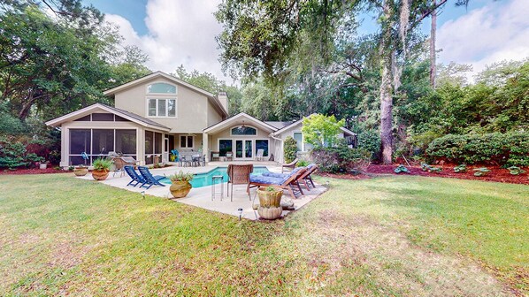A two-story house with a backyard featuring a swimming pool, lounge chairs, and a patio area.