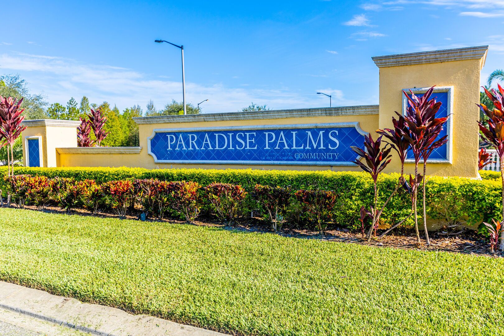 Skilt for Paradise Palms Community med velplejet græsplæne og prydplanter.