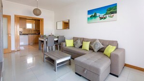 A modern living room with a grey sofa, wooden coffee table, and a dining area with a table and chairs. - Albufeira Beach Apartment with sea views of the Bay all the way to the Old Town (Albufeira)