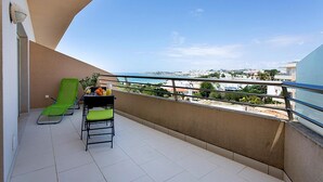 A balcony with a green chair, a table with a pitcher of orange juice, and a view of the cityscape. - Albufeira Beach Apartment with sea views of the Bay all the way to the Old Town (Albufeira)