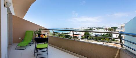 Ein Balkon mit einem grünen Stuhl, einem Tisch mit einem Krug Orangensaft und Blick auf die Stadtlandschaft.