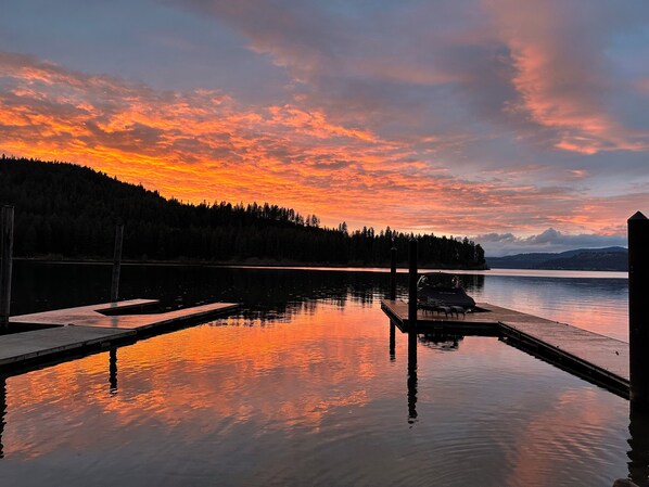 A serene lakeside view with a dock and a boat, surrounded by forested hills. - Lakefront Cabin in Carey Bay (Worley)