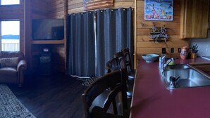 A cozy cabin interior with a leather sofa, a small round table, and a kitchen area with a sink and utensils.