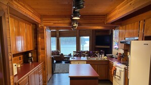 A wooden cabin kitchen with a central island, wooden cabinets, a built-in oven, and a large window overlooking a lake.