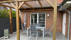 Een overdekt terras met een bakstenen muur, een raam en een deur.
