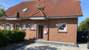 Een herenhuis met twee verdiepingen, gevel van baksteen en een dak van rode tegels, met een voordeur en een klein portaal.