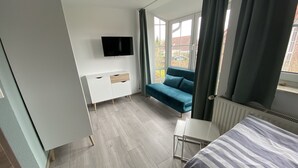 Een moderne slaapkamer met een bed, een bank, een tv aan de muur en een raam met gordijnen.