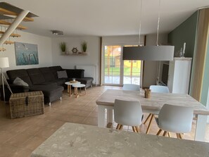 Un salon moderne avec un canapé de couleur foncée, une petite table ronde et un coin repas comprenant une table et des chaises blanches.