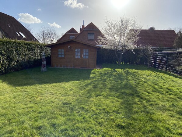 Une maison en bois avec un toit en pente, une cour clôturée et un ciel dégagé.