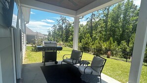 Un patio couvert équipé d’un barbecue, de mobilier d’extérieur et offrant une vue sur la verdure environnante.