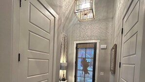 Un couloir avec des portes blanches, un tapis à motifs, un lustre allumé et une porte dotée d’un écran qui affiche une silhouette.