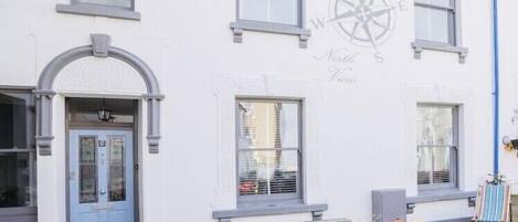 Un bâtiment orné d’une fresque représentant une boussole, avec une porte bleue et un banc à l’extérieur.