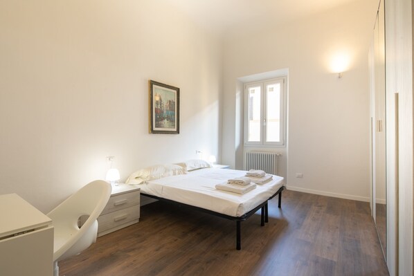 A bedroom with a bed, bedside table, chair, and a window with a radiator. - Indipendenza House by Mmega (Florence)