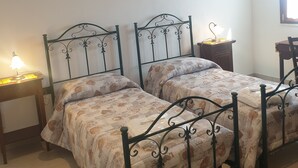 Ein Schlafzimmer mit zwei Betten mit Metallgestellen, einem Nachttisch mit Lampe, einem hölzernen Schminktisch und einem gemusterten Teppich.