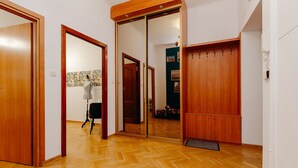 A hallway with wooden flooring, a mirrored closet door, and a chair in the background. - ShortStayPoland Piwna B25 (Warsaw)