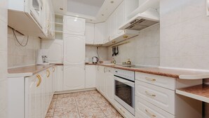 A modern kitchen with white cabinets, gold handles, a built-in oven, and a granite countertop. - ShortStayPoland Piwna B25 (Warsaw)
