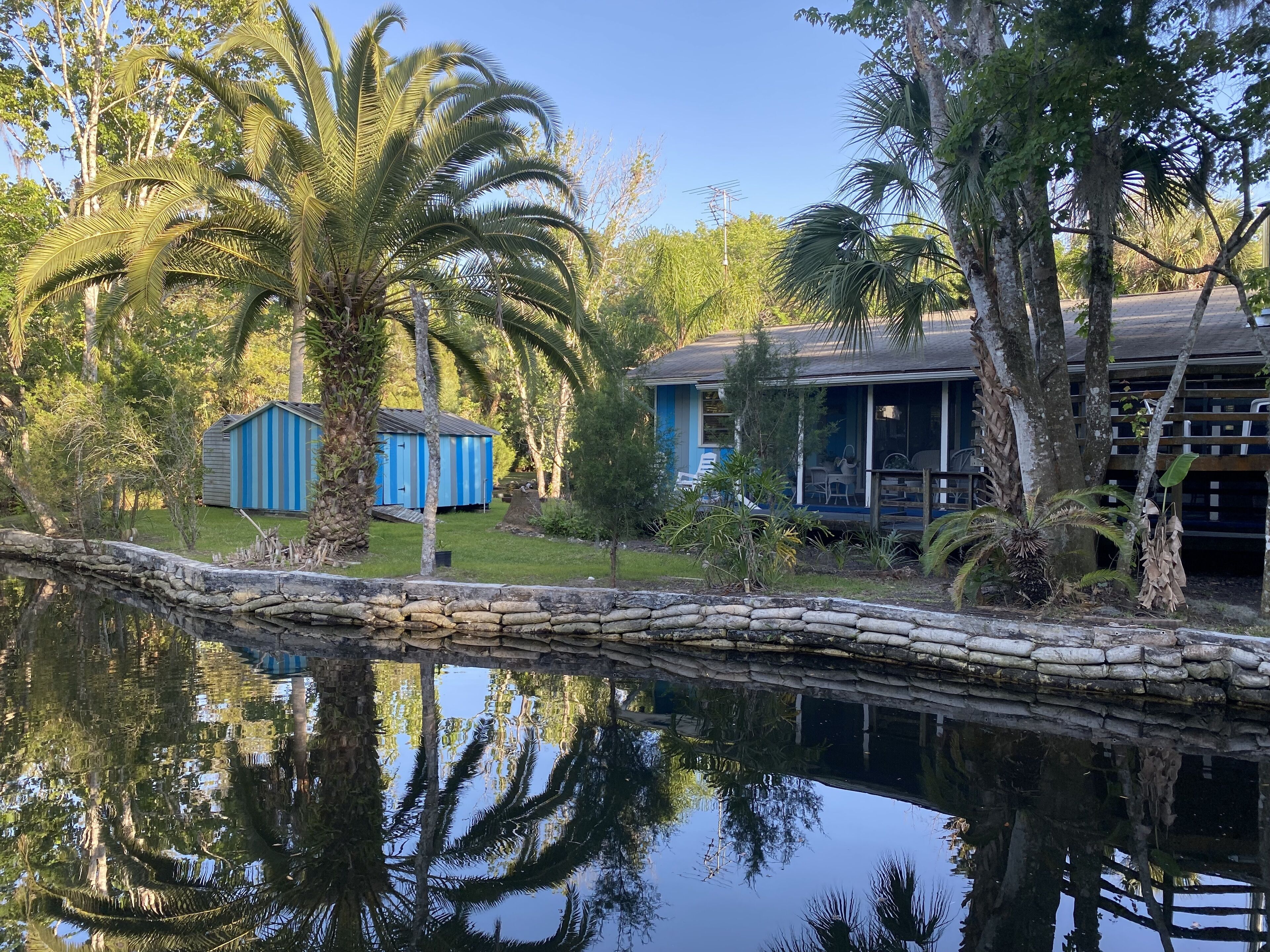 A house with a porch, a small shed, and a pond reflecting trees.