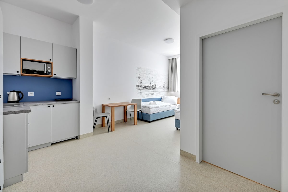 Ein moderner, minimalistischer Raum mit Küchenzeile, Bett und Schreibtisch.