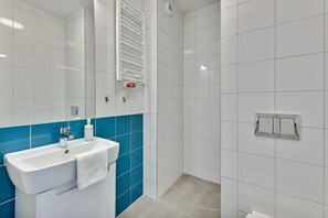 A bathroom with a white sink, blue tiles, a towel, and a shower area. - Apartgdynia (Gdynia)