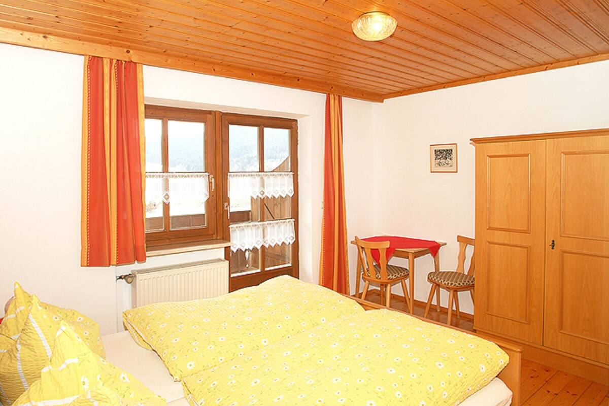 Ein Schlafzimmer mit einem Bett, einem Fenster mit Vorhängen, einem Holzschrank und einem kleinen Tisch mit Stühlen.