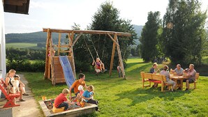 A wooden swing set and a slide in a grassy outdoor area with a bench and table nearby. - Exenbacher Hof - Pension (Arnbruck)