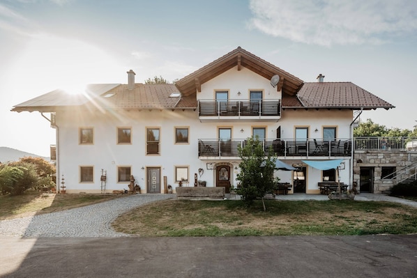 A two-story building with a balcony, a stone facade, and a paved entrance area. - Exenbacher Hof - Pension (Arnbruck)