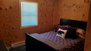 A wooden-paneled room with a bed, a window, and a radiator. - Private cabin with direct ATV/UTV trail access (Fairchild)