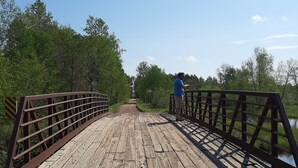 A wooden pedestrian bridge with metal railings, surrounded by greenery and a clear sky. - Private cabin with direct ATV/UTV trail access (Fairchild)