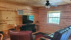 A cozy cabin interior with a wooden interior, a ceiling fan, a large TV, a leather sofa, and a fireplace. - Private cabin with direct ATV/UTV trail access (Fairchild)