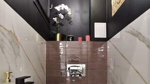 Un bagno moderno con lavandino bianco, rubinetto nero e un water. Sopra il lavandino c'è un lampadario e a parete uno specchio.